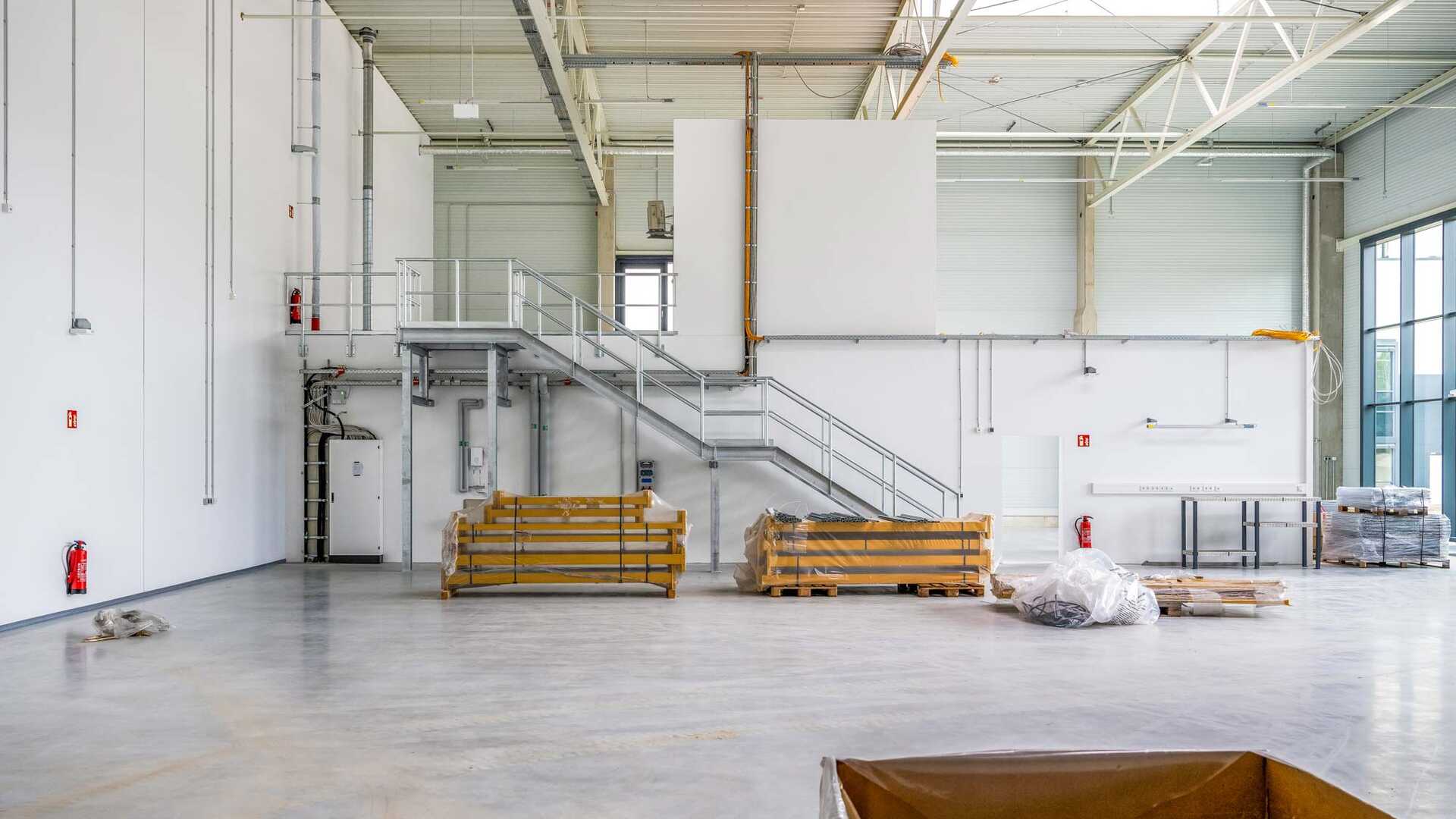 Photograph from the construction process of the railway track complex. It shows a large hall with high ceilings and a staircase to an open first floor, with building utensils lying on the floor.