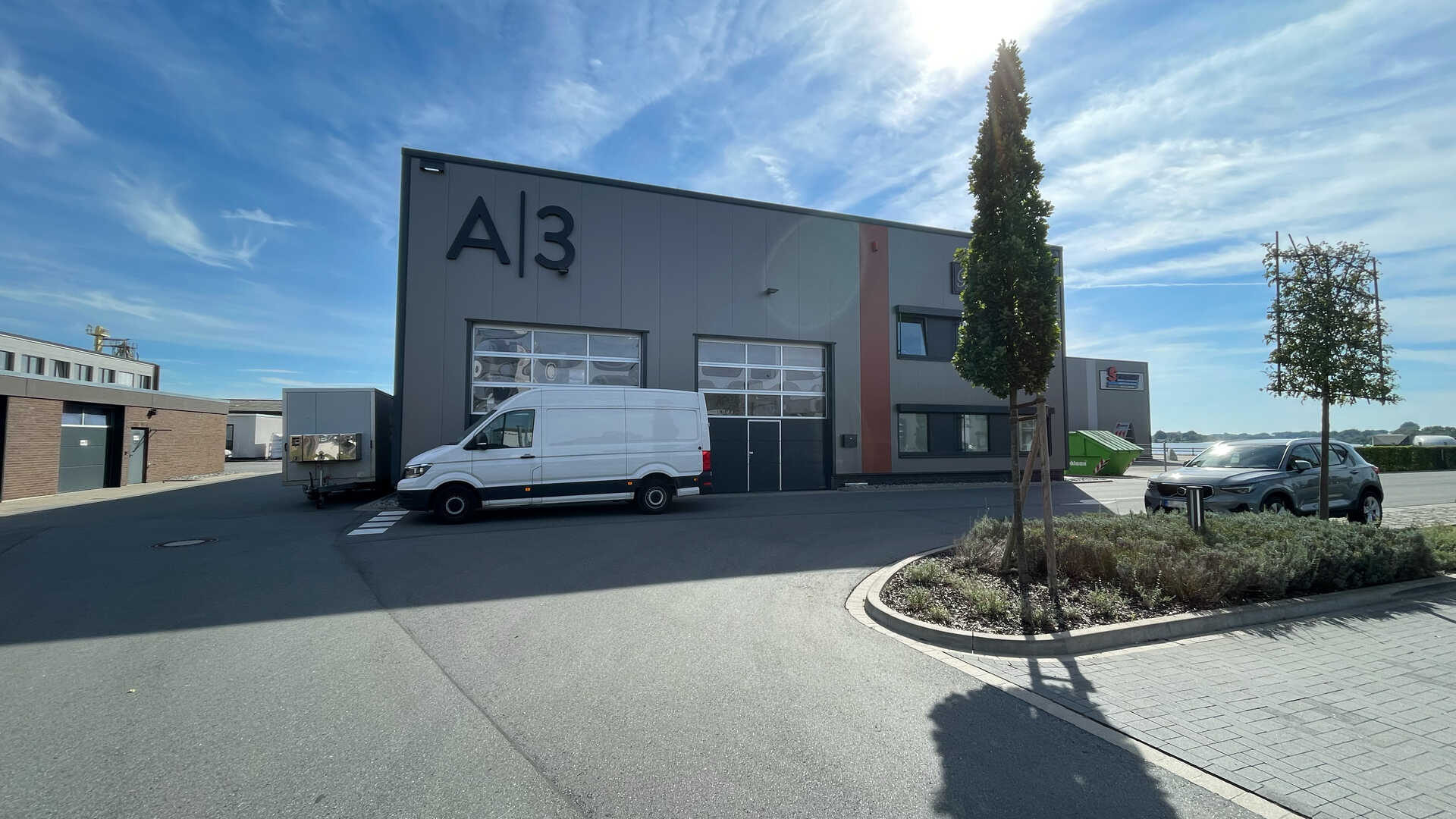 Foto der Halle A3 am Allerkai. Abgebildet ist eine Lagerhalle mit zwei großen Garagen und einem weißen Sprinter davor.